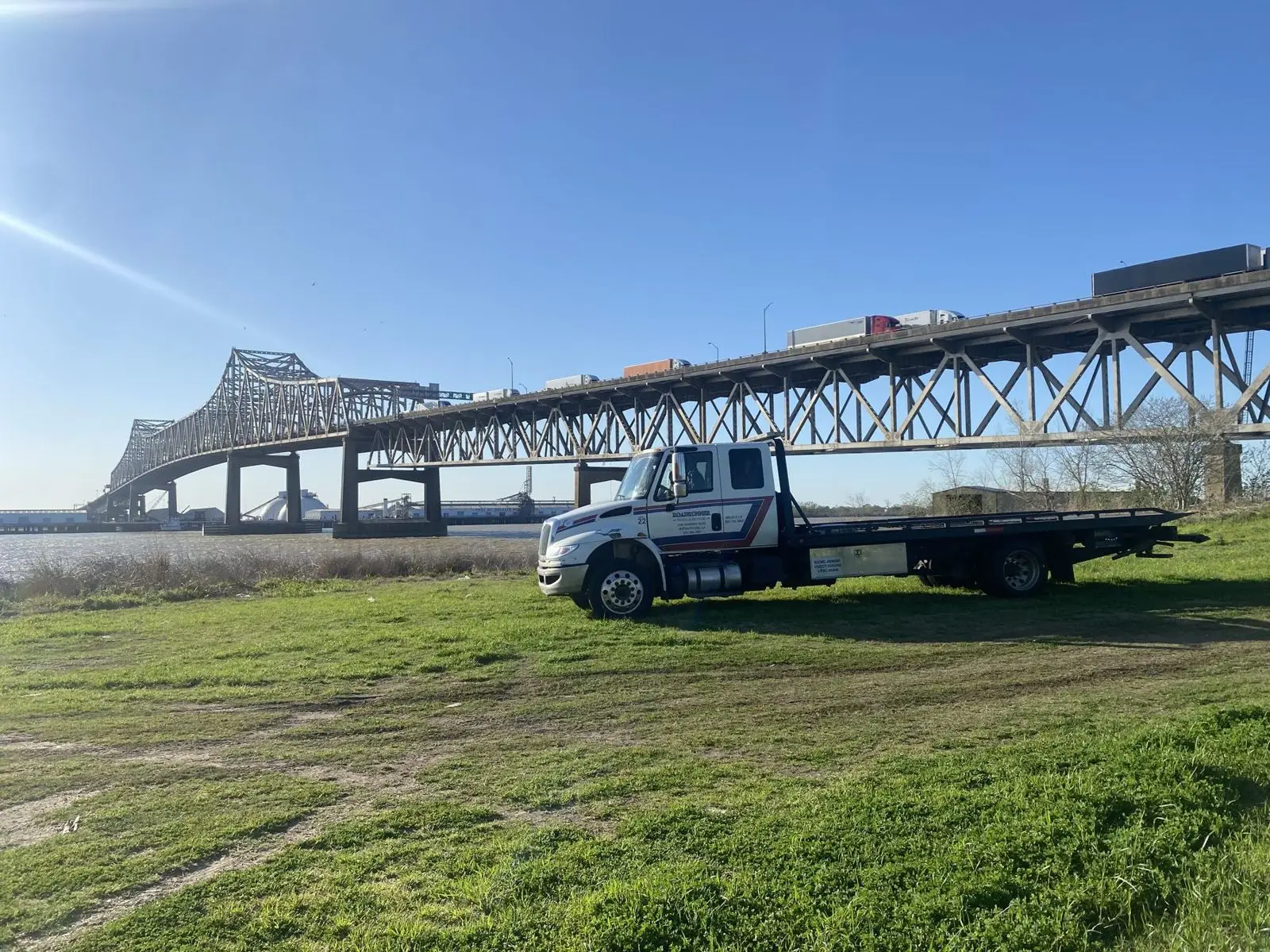 A Roadrunner light-duty flatbed tow truck in front of the Mississippi River Bridge in Baton Rouge